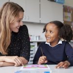 Young female teaching assistant working one to one with primary school child - career progression through gaining HLTA status